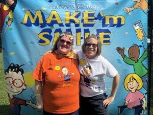 two young women smiling in front of backdrop poster